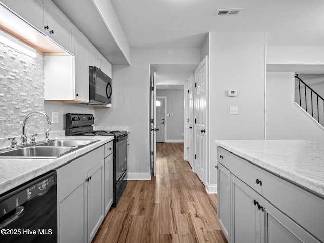 kitchen with sink, black appliances, white cabinets, and light wood-type flooring