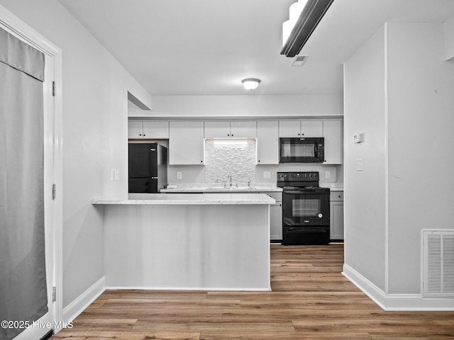 kitchen featuring sink, black appliances, light hardwood / wood-style floors, and white cabinets