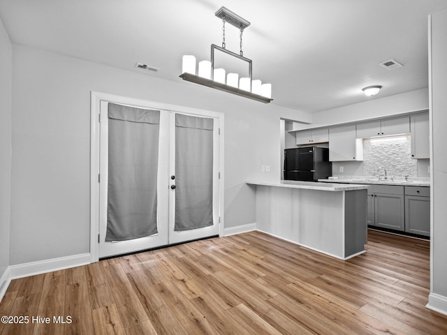 kitchen featuring gray cabinetry, black fridge, hanging light fixtures, light wood-type flooring, and kitchen peninsula