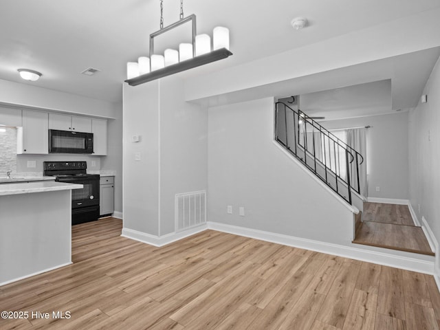 kitchen with white cabinetry, decorative light fixtures, black appliances, and light hardwood / wood-style floors