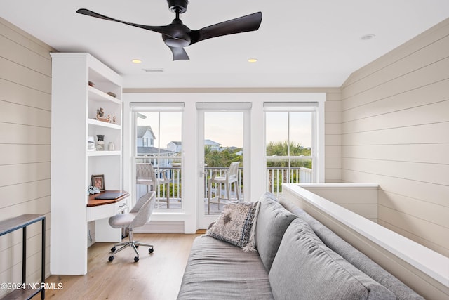 interior space with ceiling fan, light wood-type flooring, access to exterior, wood walls, and lofted ceiling