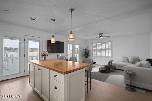 kitchen with wood counters, a breakfast bar area, a center island, hanging light fixtures, and white cabinets