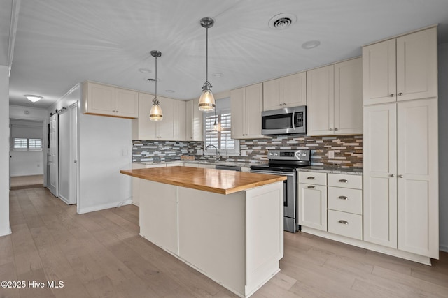 kitchen with appliances with stainless steel finishes, decorative light fixtures, white cabinetry, a center island, and a barn door