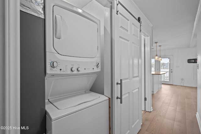 clothes washing area featuring stacked washer and dryer, a barn door, and light hardwood / wood-style flooring