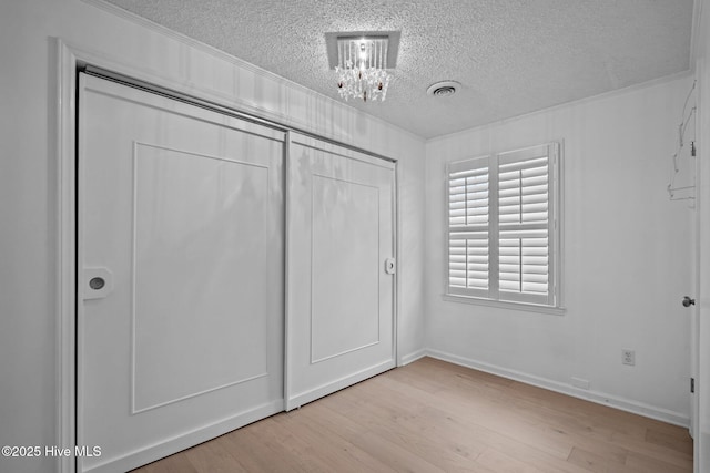 unfurnished bedroom with a closet, a notable chandelier, light hardwood / wood-style flooring, and a textured ceiling