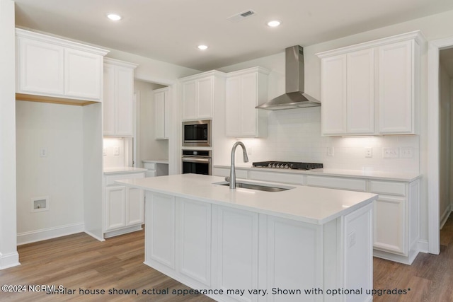 kitchen with sink, stainless steel appliances, an island with sink, and wall chimney exhaust hood