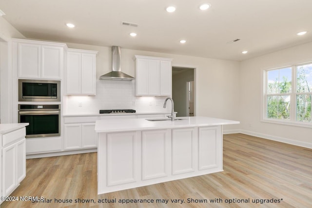 kitchen featuring built in microwave, wall chimney range hood, an island with sink, and stainless steel oven