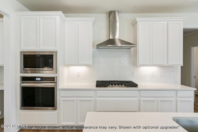 kitchen with white cabinetry, appliances with stainless steel finishes, and wall chimney range hood