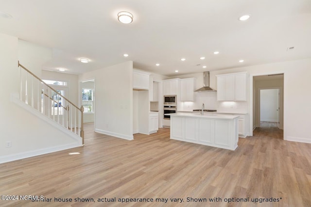 kitchen featuring stainless steel appliances, a center island with sink, white cabinets, and wall chimney exhaust hood