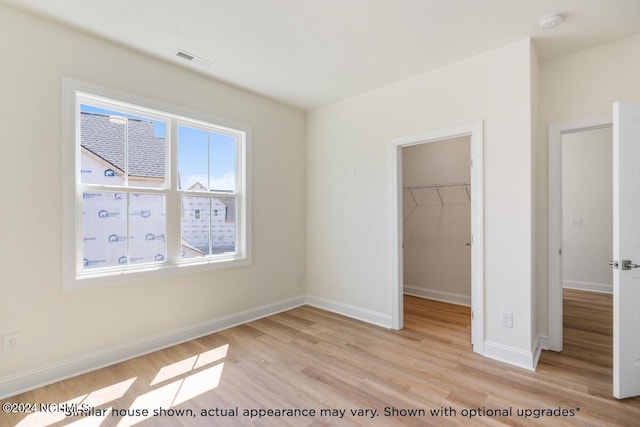 unfurnished bedroom with a walk in closet, a closet, and light wood-type flooring