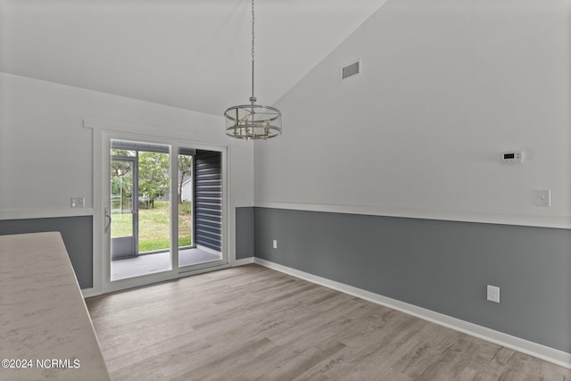 unfurnished dining area with an inviting chandelier, high vaulted ceiling, and light hardwood / wood-style flooring