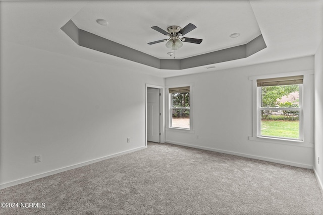 carpeted empty room with ceiling fan, a raised ceiling, and a wealth of natural light