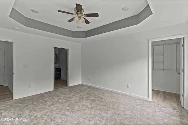 unfurnished bedroom featuring light colored carpet, a tray ceiling, ensuite bath, and a spacious closet