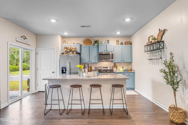 kitchen with a kitchen bar, a kitchen island with sink, a sink, blue cabinetry, and appliances with stainless steel finishes