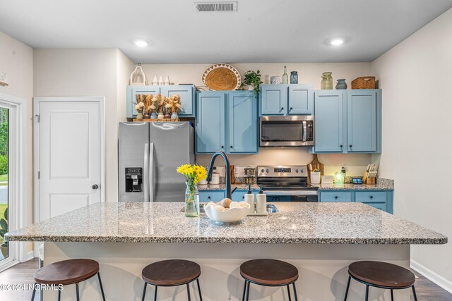 kitchen with an island with sink, stainless steel appliances, blue cabinetry, and a breakfast bar area