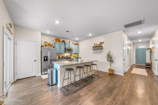 kitchen with dark wood-type flooring, appliances with stainless steel finishes, an island with sink, and a breakfast bar