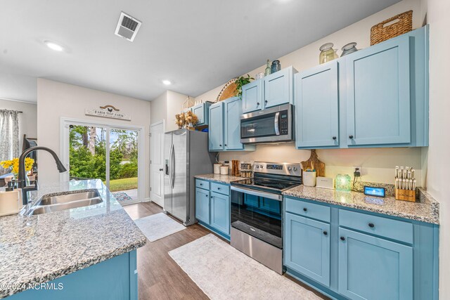 kitchen featuring light stone countertops, stainless steel appliances, dark hardwood / wood-style flooring, sink, and blue cabinets