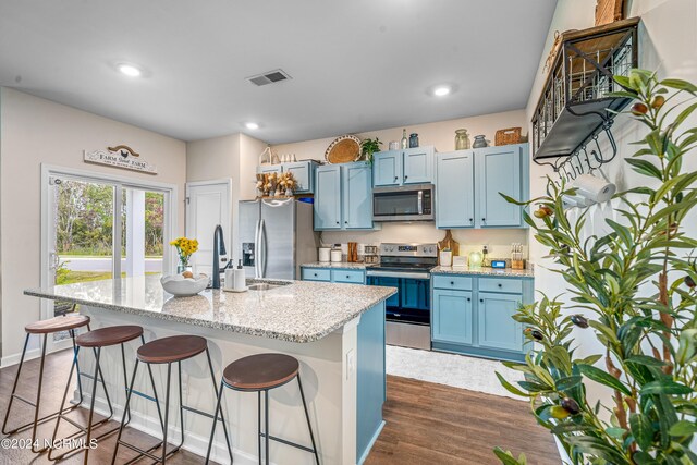 kitchen with blue cabinetry, a kitchen bar, stainless steel appliances, dark hardwood / wood-style flooring, and a center island with sink