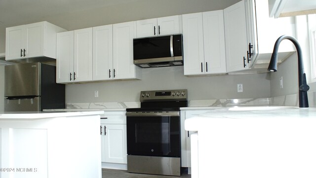 kitchen featuring appliances with stainless steel finishes, light stone counters, and white cabinetry