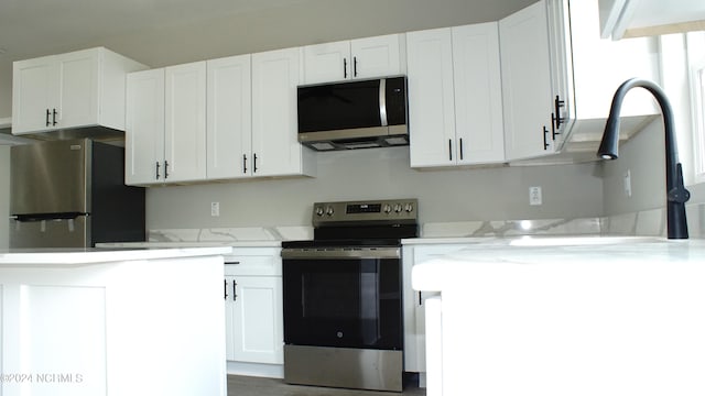 kitchen featuring a sink, appliances with stainless steel finishes, white cabinets, and light stone counters