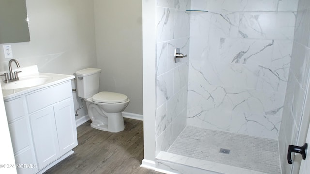 bathroom with wood-type flooring, toilet, a tile shower, and vanity