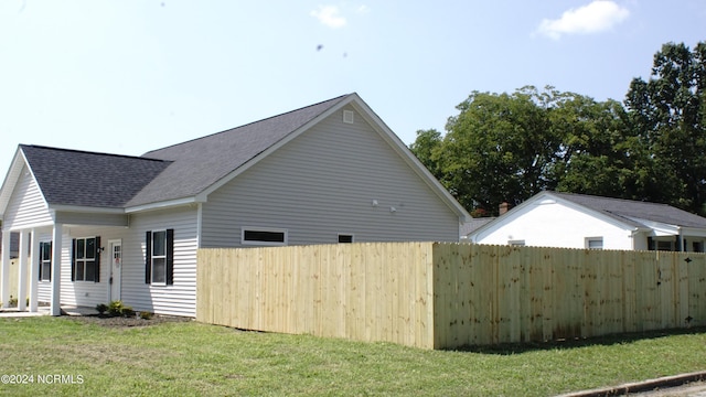 view of home's exterior featuring roof with shingles, a yard, and fence