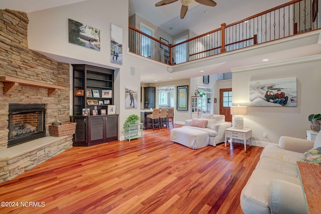 living room featuring built in features, hardwood / wood-style flooring, a fireplace, ceiling fan, and a towering ceiling