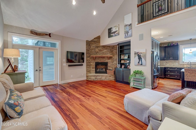 living room with a fireplace, high vaulted ceiling, built in features, french doors, and light hardwood / wood-style flooring