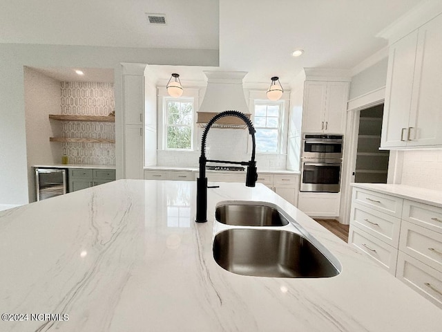 kitchen featuring white cabinetry, sink, beverage cooler, stainless steel double oven, and light stone counters