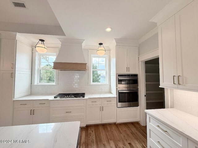 kitchen with white cabinets, decorative backsplash, custom range hood, and appliances with stainless steel finishes