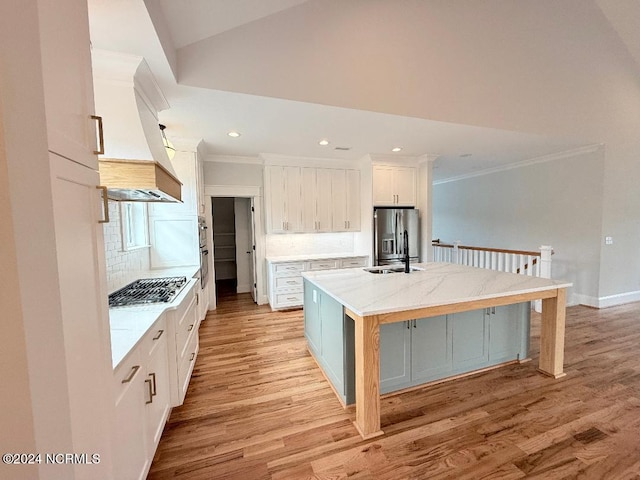 kitchen with appliances with stainless steel finishes, light wood-type flooring, tasteful backsplash, white cabinets, and an island with sink