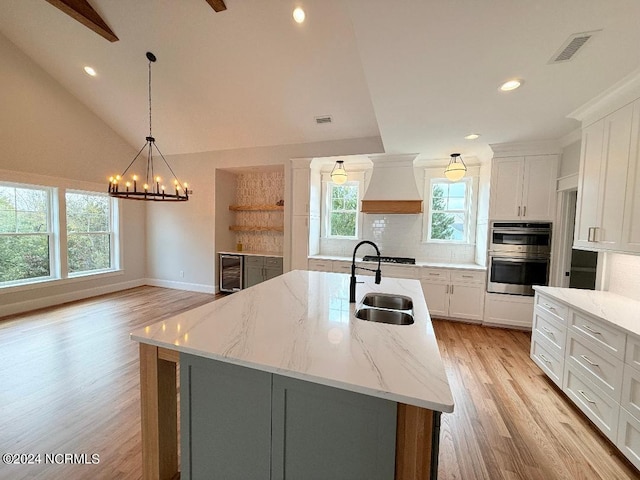 kitchen featuring custom exhaust hood, a kitchen island with sink, sink, light hardwood / wood-style flooring, and white cabinets