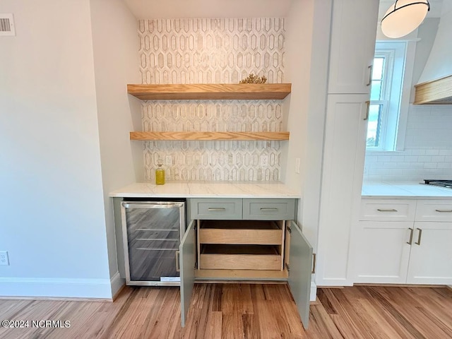 bar featuring ventilation hood, wine cooler, light hardwood / wood-style flooring, decorative backsplash, and white cabinetry