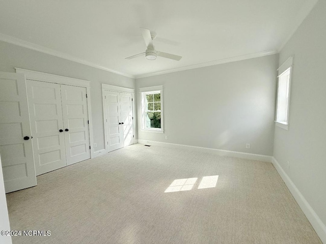 unfurnished bedroom with ceiling fan, light colored carpet, ornamental molding, and multiple closets