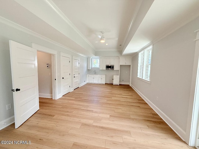 unfurnished living room featuring ceiling fan, sink, ornamental molding, and light wood-type flooring