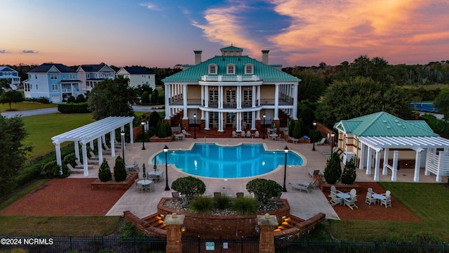 pool at dusk featuring a pergola and a patio area