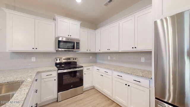 kitchen featuring light wood finished floors, stainless steel appliances, visible vents, backsplash, and white cabinets