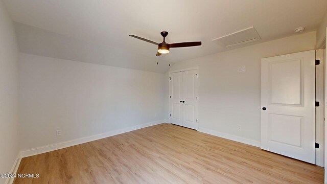 unfurnished bedroom featuring lofted ceiling, a closet, attic access, light wood-type flooring, and baseboards