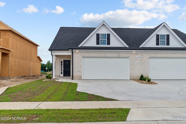 view of front of property featuring brick siding, roof with shingles, a front yard, a garage, and driveway