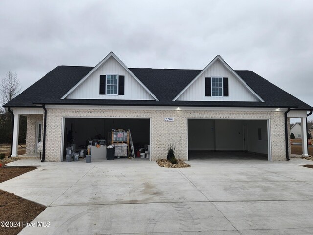 view of front of house featuring driveway, brick siding, and roof with shingles