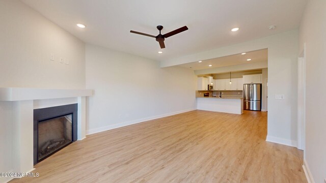 unfurnished living room featuring light wood finished floors, baseboards, a ceiling fan, a fireplace, and recessed lighting