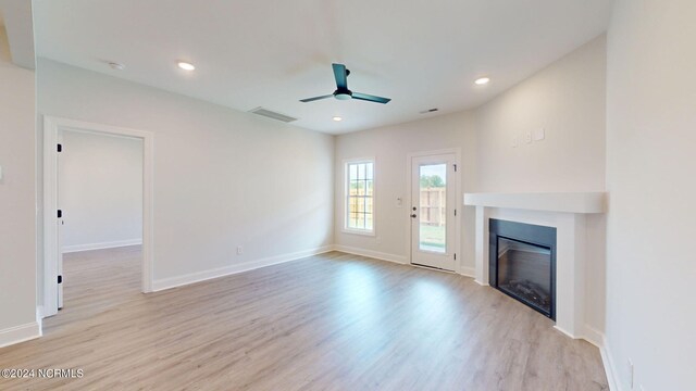 unfurnished living room with a glass covered fireplace, baseboards, recessed lighting, and wood finished floors