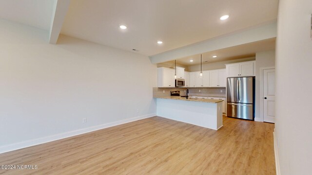 kitchen featuring light wood-style flooring, a peninsula, white cabinets, appliances with stainless steel finishes, and tasteful backsplash