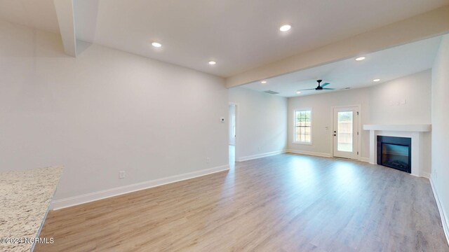 unfurnished living room with baseboards, a ceiling fan, a glass covered fireplace, light wood-style flooring, and recessed lighting