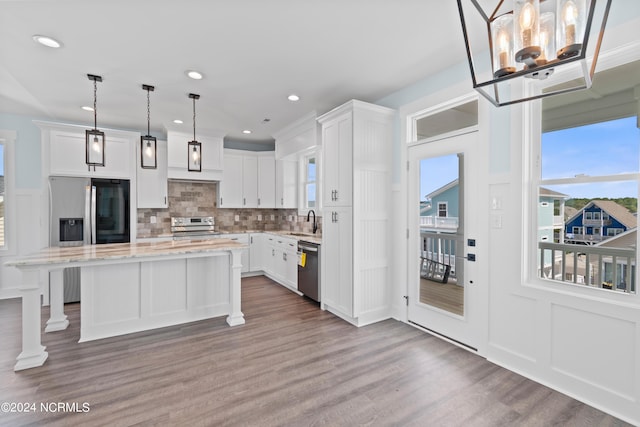 kitchen featuring wood-type flooring, decorative light fixtures, white cabinets, appliances with stainless steel finishes, and a center island