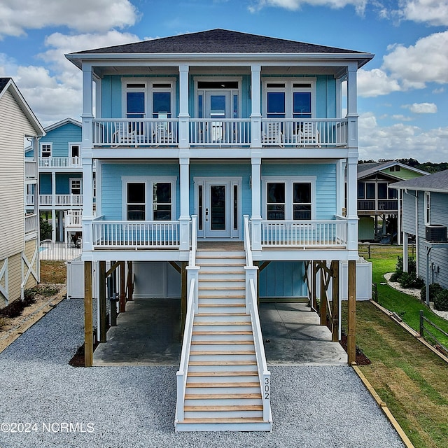 coastal home with central AC unit, a balcony, a front lawn, and a carport