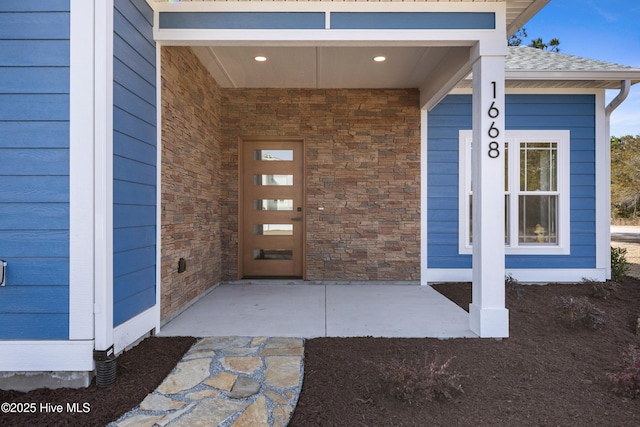 property entrance featuring a shingled roof and stone siding