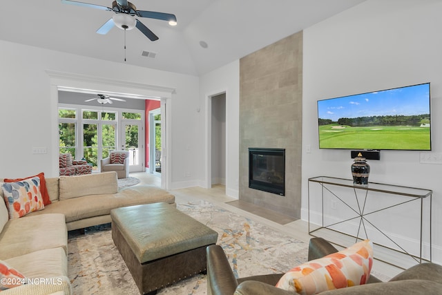 living room featuring ceiling fan, vaulted ceiling, and a tiled fireplace