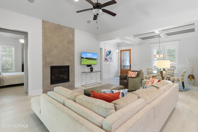 living room with a tile fireplace, coffered ceiling, ceiling fan, light wood-type flooring, and beam ceiling