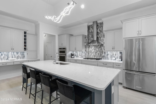 kitchen with a center island with sink, wall chimney exhaust hood, light stone counters, and appliances with stainless steel finishes